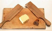 Photo of butter pats on a wooden board. The butter pats are rectangular wooden paddles with handles.